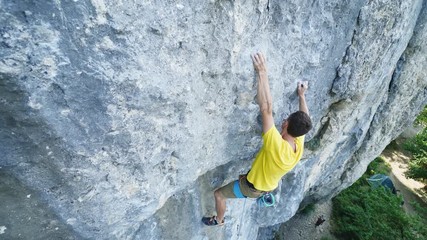 top view of man rock climber in yellow t-shirt, climbing on a cliff, searching, reaching and gripping hold, attaching rope. outdoors rock climbing and active lifestyle concept, 4K stock footage
