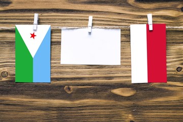 Hanging flags of Djibouti and Monaco attached to rope with clothes pins with copy space on white note paper on wooden background.Diplomatic relations between countries.