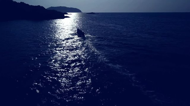 Refugee or human trafficking motor boat in the waves at night at sea, crowded and full of escaping immigrants, people or illegal drugs. Going closer to the shore or land