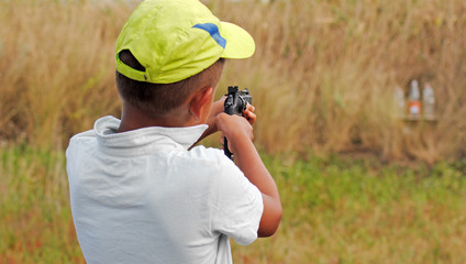A boy in a cap with gun shoots at objects. Sports weapon in the hands of a minor child.
