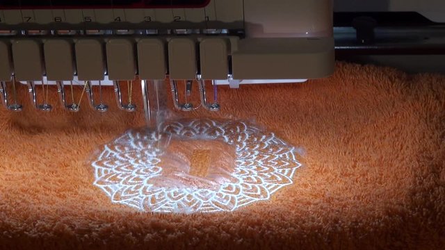 Machine embroidery of the monogram of the letter "D" in the mandala on a terry orange towel fabric inserted into the hoop