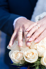 Obraz na płótnie Canvas hands of the bride and groom at the wedding with wedding rings on the background of a bouquet of roses