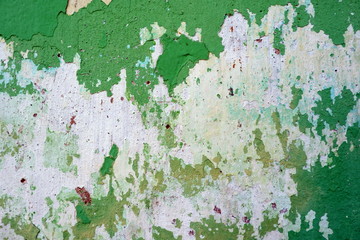 Old weathered painted wall background texture. Green dirty peeled plaster wall with falling off flakes of paint.Peeling paint on a metal surface.Cracked paint damaged concrete rough texture.