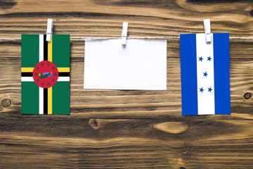 Hanging flags of Dominica and Honduras attached to rope with clothes pins with copy space on white...