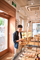 Handsome man at the local bakery store holding a tray with buns or pies buying eating dessert...