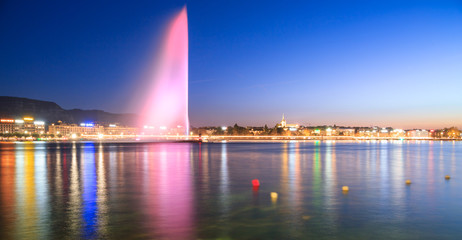 Geneva city lights at night . Pink fountain is reflected in still lake in the evening. Colorful...