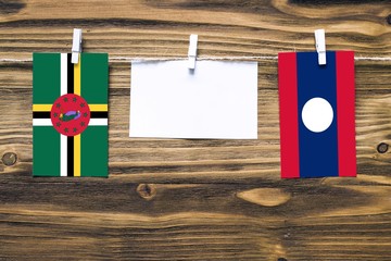 Hanging flags of Dominica and Laos attached to rope with clothes pins with copy space on white note paper on wooden background.Diplomatic relations between countries.
