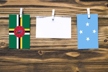 Hanging flags of Dominica and Micronesia attached to rope with clothes pins with copy space on white note paper on wooden background.Diplomatic relations between countries.
