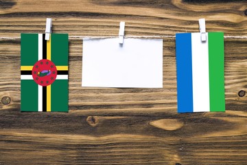 Hanging flags of Dominica and Sierra Leone attached to rope with clothes pins with copy space on white note paper on wooden background.Diplomatic relations between countries.