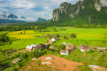 Fototapeta na wymiar Aerial view of green rice fields and mountains, paddy field at Vang Vieng , Laos. Southeast Asia. Photo made by drone from above. Bird eye view.