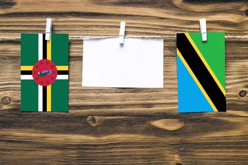 Hanging flags of Dominica and Tanzania attached to rope with clothes pins with copy space on white note paper on wooden background.Diplomatic relations between countries.