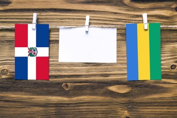 Hanging flags of Dominican Republic and Gabon attached to rope with clothes pins with copy space on white note paper on wooden background.Diplomatic relations between countries.