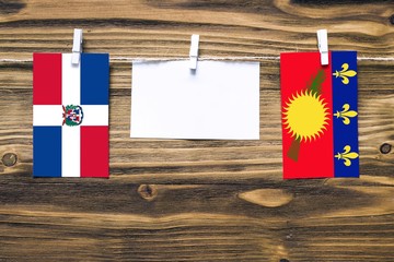 Hanging flags of Dominican Republic and Guadeloupe attached to rope with clothes pins with copy space on white note paper on wooden background.Diplomatic relations between countries.