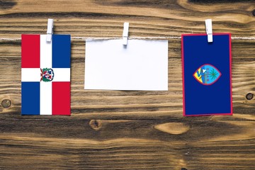 Hanging flags of Dominican Republic and Guam attached to rope with clothes pins with copy space on white note paper on wooden background.Diplomatic relations between countries.