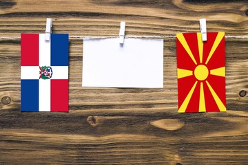 Hanging flags of Dominican Republic and Macedonia attached to rope with clothes pins with copy space on white note paper on wooden background.Diplomatic relations between countries.