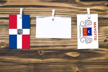 Hanging flags of Dominican Republic and Mayotte attached to rope with clothes pins with copy space on white note paper on wooden background.Diplomatic relations between countries.