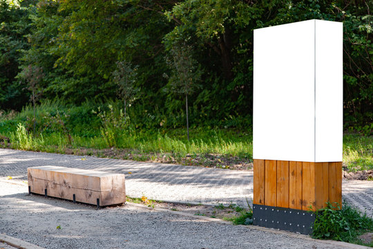 Blank vertical information sign in park on wooden stand in front green forest