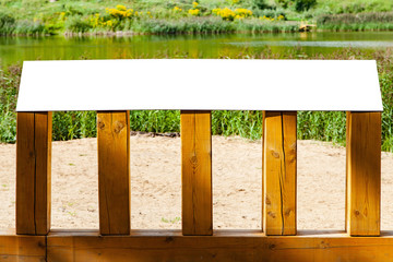 Blank horizontal information sign in park in front of a lake on wooden stand