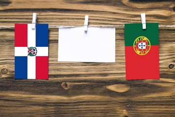 Hanging flags of Dominican Republic and Portugal attached to rope with clothes pins with copy space on white note paper on wooden background.Diplomatic relations between countries.