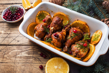 Baked chicken drumstick with oranges and cranberries in a baking sheet on a wooden background. Christmas food Table with decorations.
