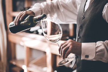 Sommelier Concept. Senior man standing pouring wine into glass close-up