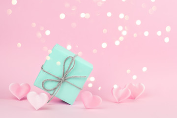 Gift box of blue color decorated with a string of twine on a pink background among pink silk hearts. Holiday concept. Place for text.