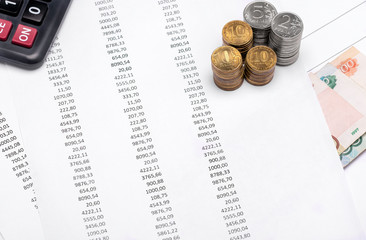 Close-up printed numbers on white paper, on which lies the calculator, coins of different values of rubles and next to paper bills.