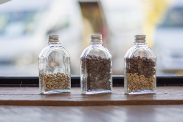 Raw coffee beans in bottles on a wooden table with indoor lighting.