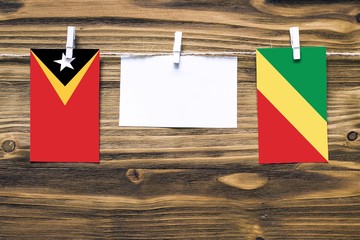 Hanging flags of East Timor and Republic Of The Congo attached to rope with clothes pins with copy space on white note paper on wooden background.Diplomatic relations between countries.