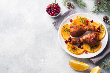 Baked chicken drumstick with oranges and cranberries in a plate light grey background. Christmas food Table with decorations. Copy space.