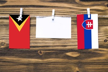 Hanging flags of East Timor and Slovakia attached to rope with clothes pins with copy space on white note paper on wooden background.Diplomatic relations between countries.