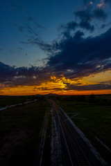 Scenic sunset over sunlit empty railway tracks and asphalt road near Krum, Southern Bulgaria, elevated view from a bridge