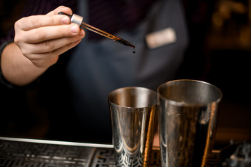 Male bartender adding a brown essence to an alcoholic drink in a steel shaker