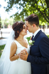 The bride and groom walk together in the park. Charming bride in a white dress, the groom is...