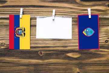 Hanging flags of Ecuador and Guam attached to rope with clothes pins with copy space on white note paper on wooden background.Diplomatic relations between countries.