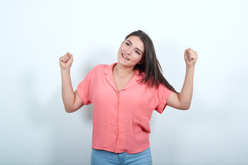 Woman on isolated vibrant white color celebrating a victory. brunette lady in pink shirt raises her...