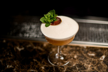 Alcoholic cocktail in the glass decorated with a mint leaf branch and dried orange slice
