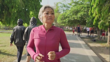 slow motion gimbal tracking shot on attractive middle aged lady running happy at city park . beautiful and sporty 40s woman exercising doing jogging workout enjoying healthy lifestyle and fitness