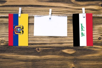 Hanging flags of Ecuador and Iraq attached to rope with clothes pins with copy space on white note paper on wooden background.Diplomatic relations between countries.