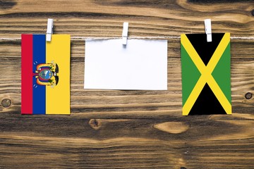 Hanging flags of Ecuador and Jamaica attached to rope with clothes pins with copy space on white note paper on wooden background.Diplomatic relations between countries.