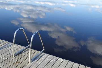 bath pontoon with boarding ladder at a finnish lake with mirrored  blue sky 