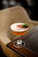 Delicious alcoholic cocktail in the glass decorated with a mint leaf, peppercorns and dried orange slice on the table