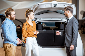 Couple with sales manager near the car in the showroom