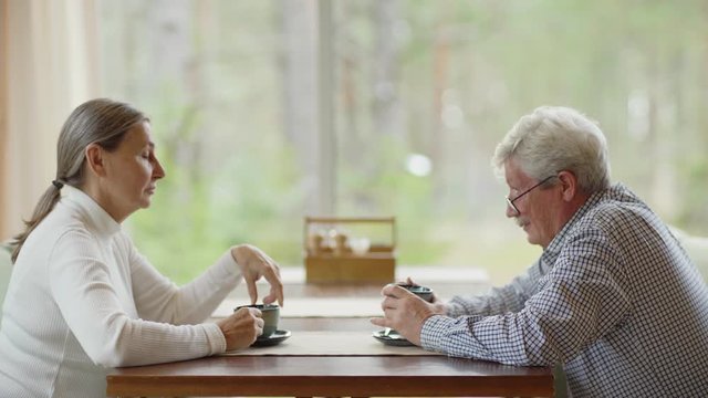 Side View Zoom In Shot Of Senior Man And Woman Sitting At Table In Cafe And Talking Over Tea Or Coffee