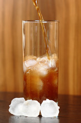 Pouring cola into glass with ice cubes