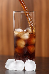 Pouring cola into glass with ice cubes