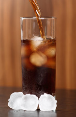 Pouring cola into glass with ice cubes