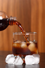 Pouring cola from plastic bottle into rocks glass with ice cubes