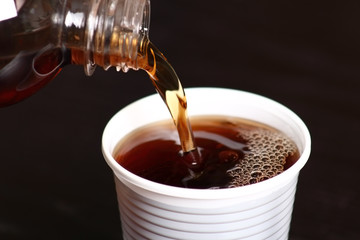 Pouring cola from bottle into plastic cup. Macro.