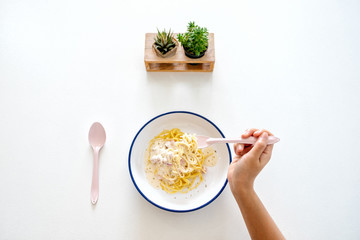 Top view image of a woman eating carbonara spaghetti on the table